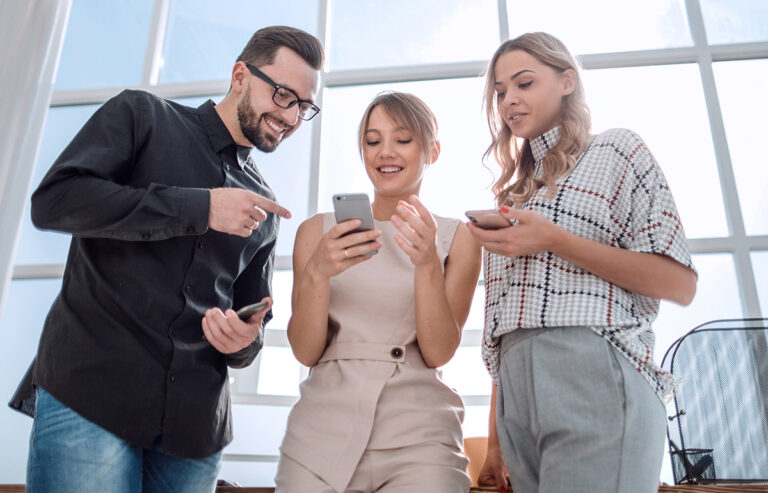 Drei Personen stehen zusammen und schauen auf Ihr Mobiltelefon