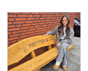 Man sieht Anna Lettow, Mitarbeiterin der Firma Wetter & Co., auf einer Bank sitzen. Anna hat lange braune Haare und lächelt in die Kamera