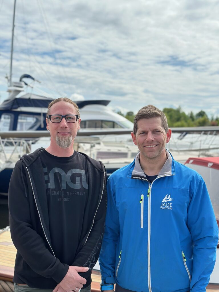 Man sieht Lutz Möller, Datenschutzbeauftragter von Die Datenschutzdenker, und Tobias Schadewaldt, Geschäftsführer von Jade Yachting. Beide sind Männer mittleren Alters und stehen vor einer Yacht.