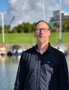 Man sieht Lutz, den (externen) Datenschutzbeauftragten von Die Datenschutzdenker. Er ist ein Mann mittleren Alters mit langen, zurückgebunden Haaren und Brille.